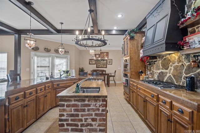 kitchen with sink, beam ceiling, decorative light fixtures, stainless steel gas stovetop, and an island with sink