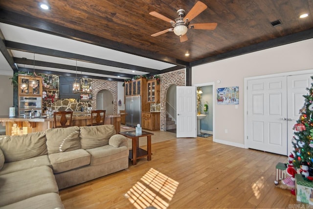 living room with light wood-type flooring, brick wall, ceiling fan with notable chandelier, beam ceiling, and wooden ceiling