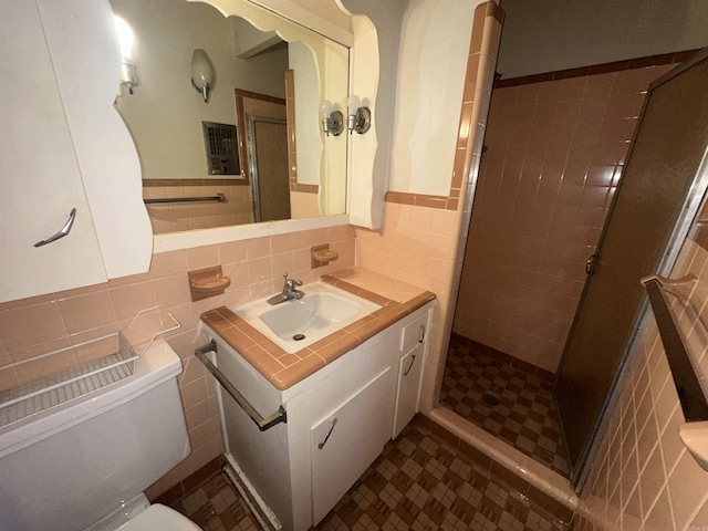 bathroom with vanity, toilet, a shower with shower door, and tile walls