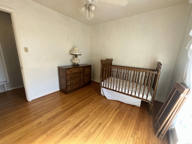 bedroom with ceiling fan, light hardwood / wood-style floors, and a crib