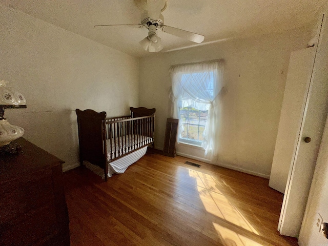 bedroom featuring ceiling fan, a crib, and hardwood / wood-style flooring