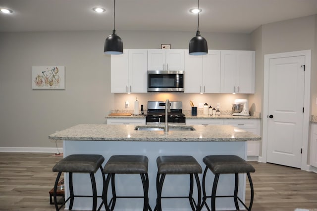 kitchen with light stone countertops, stainless steel appliances, white cabinetry, and an island with sink