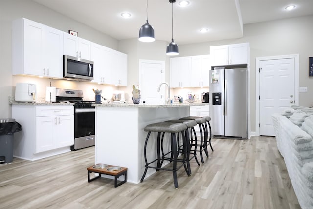 kitchen featuring white cabinetry, light hardwood / wood-style floors, decorative light fixtures, a center island with sink, and appliances with stainless steel finishes