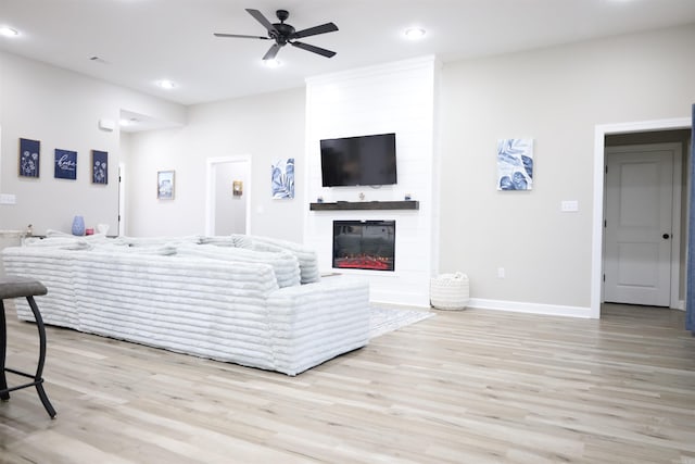 living room with ceiling fan, a fireplace, and light hardwood / wood-style floors