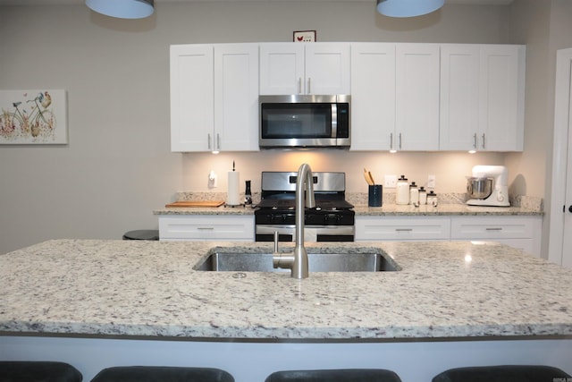 kitchen featuring a breakfast bar, appliances with stainless steel finishes, white cabinetry, and light stone counters