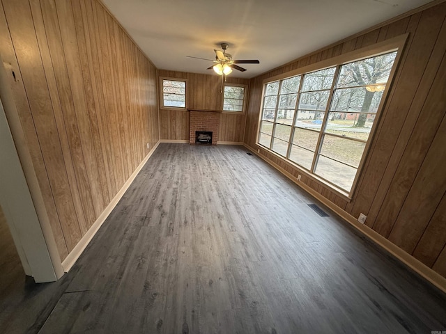 unfurnished room with a fireplace, ceiling fan, and wooden walls