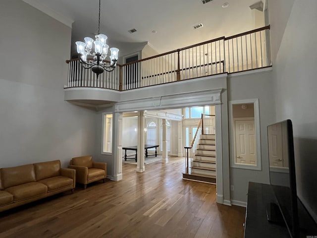 unfurnished living room with a high ceiling, ornamental molding, a notable chandelier, and hardwood / wood-style floors