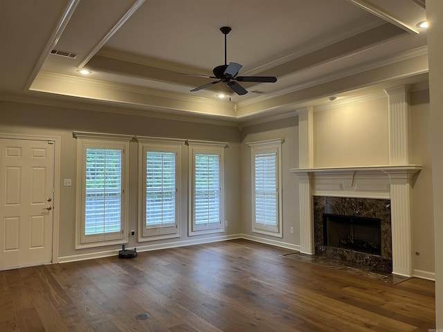 unfurnished living room featuring ceiling fan, dark hardwood / wood-style flooring, a high end fireplace, a tray ceiling, and ornamental molding