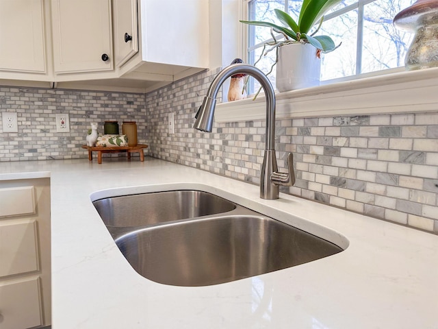 details featuring tasteful backsplash, light stone counters, and sink