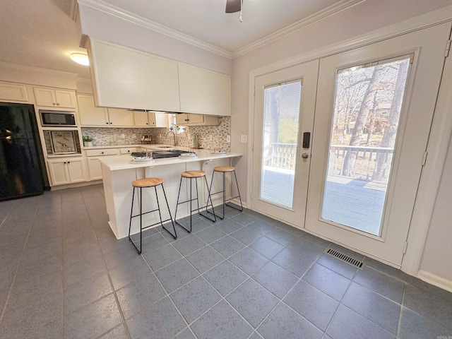 kitchen featuring a breakfast bar, stainless steel microwave, black refrigerator, white cabinetry, and kitchen peninsula