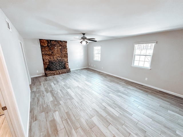 unfurnished living room with ceiling fan, a stone fireplace, and light hardwood / wood-style flooring