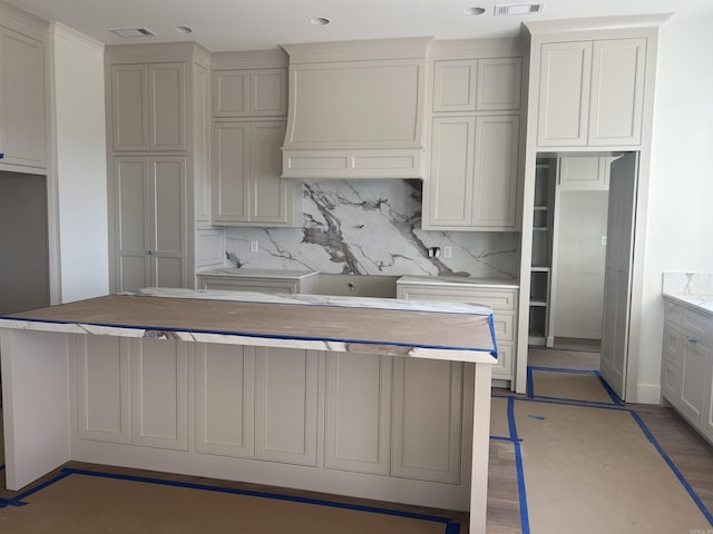 kitchen featuring hardwood / wood-style floors, premium range hood, gray cabinetry, and backsplash