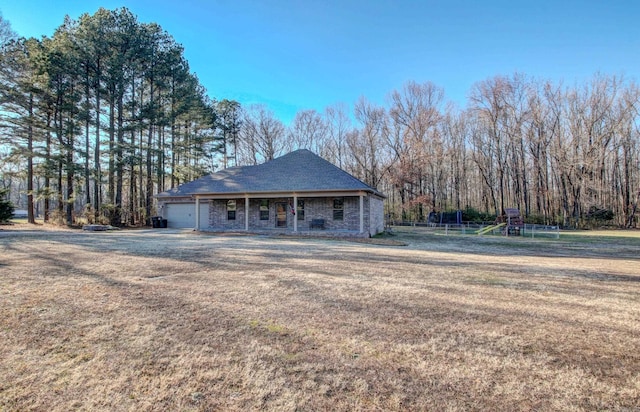 view of front of home featuring a playground, covered porch, a front yard, and a garage