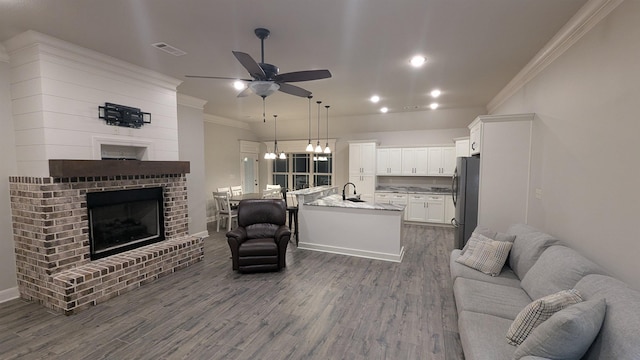 living room featuring crown molding, a brick fireplace, dark wood-type flooring, and ceiling fan with notable chandelier