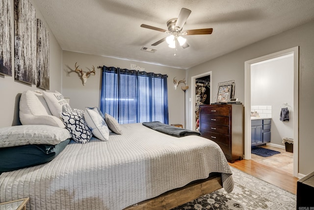 bedroom with ensuite bath, a textured ceiling, ceiling fan, hardwood / wood-style flooring, and a closet