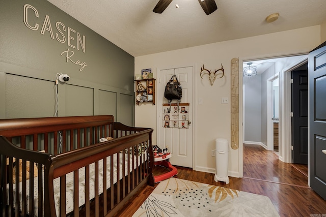 bedroom featuring ceiling fan, dark hardwood / wood-style flooring, a nursery area, and a textured ceiling