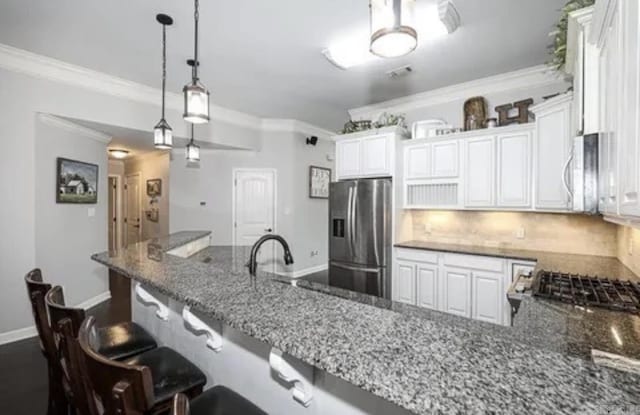 kitchen featuring backsplash, dark stone counters, stainless steel fridge, a kitchen bar, and white cabinetry