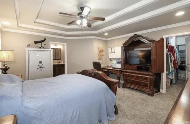 bedroom featuring a walk in closet, ensuite bath, ornamental molding, a raised ceiling, and ceiling fan