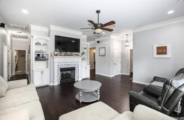 living room with ornamental molding, built in shelves, ceiling fan, dark hardwood / wood-style floors, and a tiled fireplace