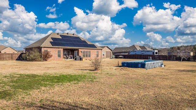 rear view of property featuring solar panels, a fenced in pool, and a yard