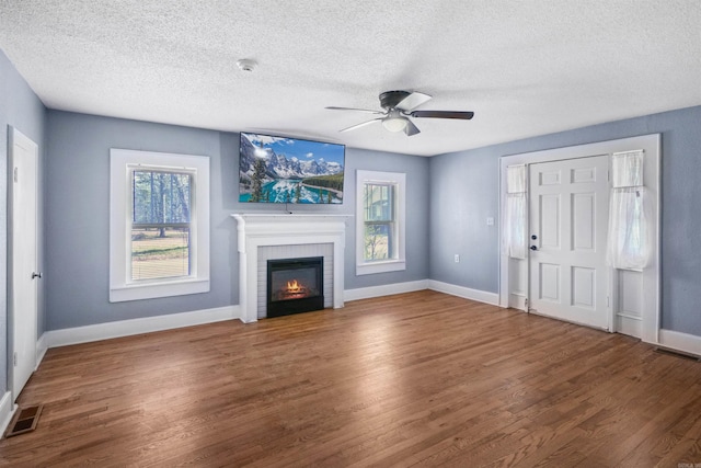 unfurnished living room with ceiling fan, hardwood / wood-style floors, a textured ceiling, and a brick fireplace