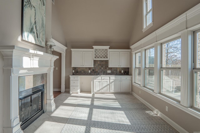 kitchen with light tile patterned floors, backsplash, a towering ceiling, a fireplace, and white cabinets