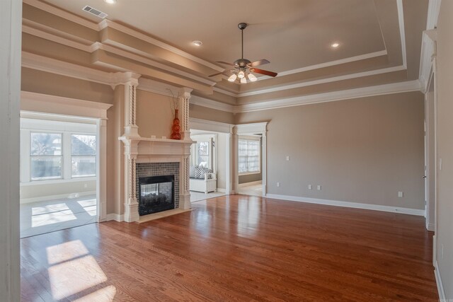 unfurnished living room featuring a tray ceiling, ceiling fan, crown molding, a fireplace, and light hardwood / wood-style floors