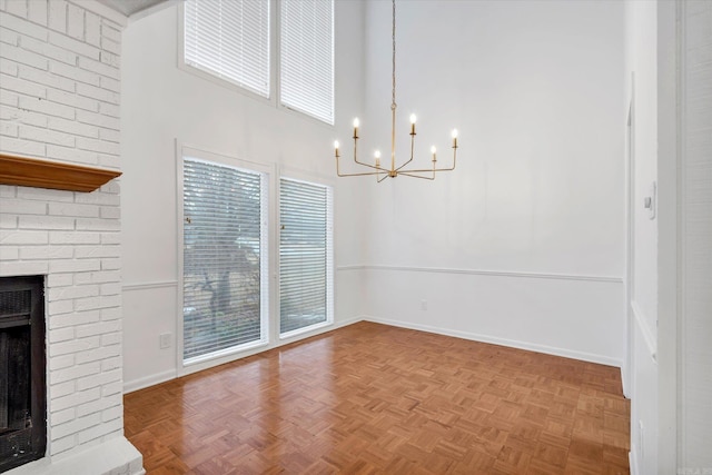 unfurnished dining area featuring a notable chandelier, parquet floors, a high ceiling, and a brick fireplace