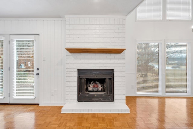 unfurnished living room with a brick fireplace, wooden walls, and baseboards