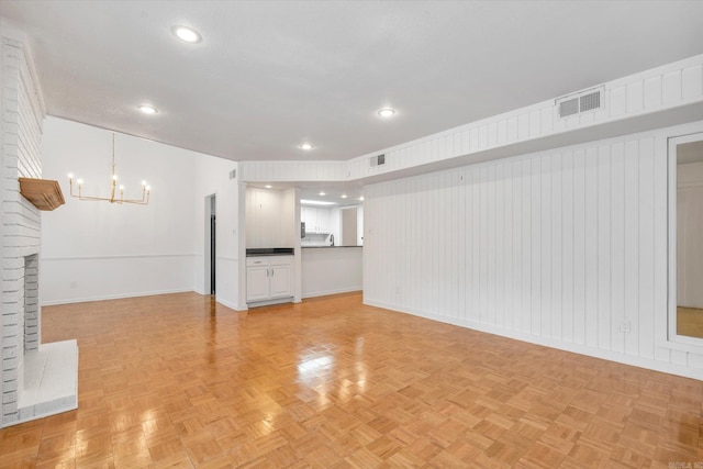 unfurnished living room featuring a brick fireplace, light parquet floors, and a notable chandelier