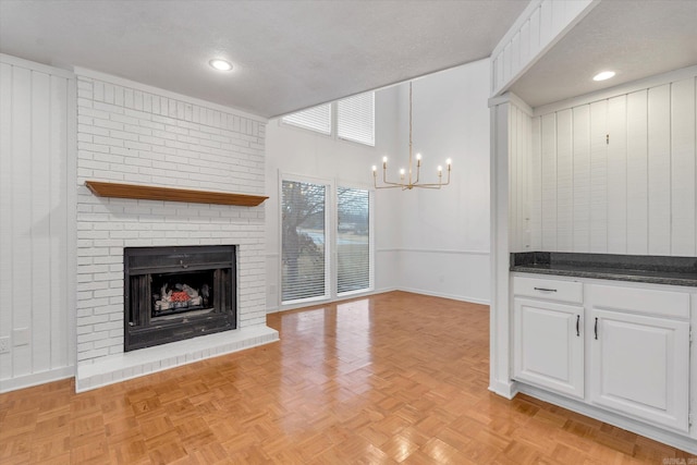 unfurnished living room with an inviting chandelier, a fireplace, baseboards, and a textured ceiling