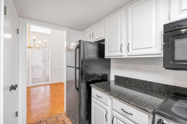 kitchen with black refrigerator, stove, a notable chandelier, dark stone countertops, and white cabinets