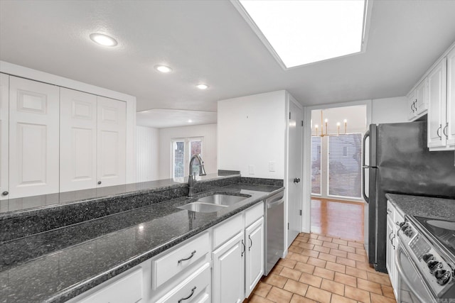 kitchen with appliances with stainless steel finishes, dark stone countertops, a sink, and white cabinetry