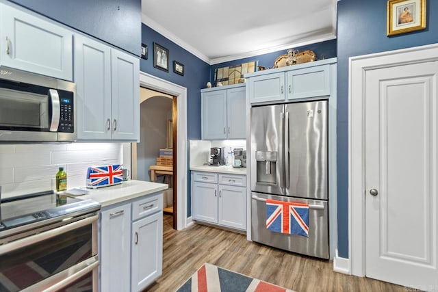 kitchen with light hardwood / wood-style flooring, decorative backsplash, ornamental molding, appliances with stainless steel finishes, and white cabinetry