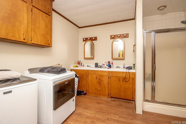 clothes washing area with washer and dryer, light wood-type flooring, and ornamental molding