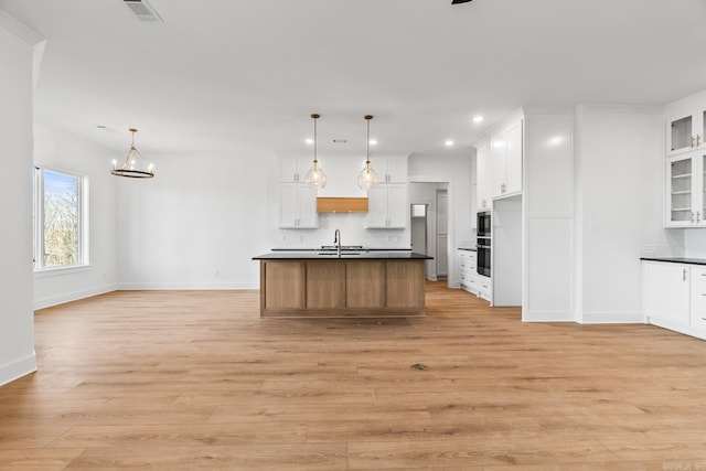 kitchen with white cabinets, pendant lighting, and a center island with sink