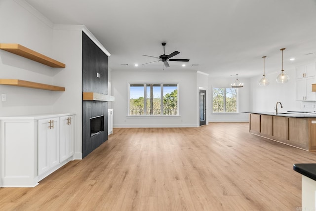 unfurnished living room featuring a fireplace, light wood-type flooring, ceiling fan with notable chandelier, and ornamental molding