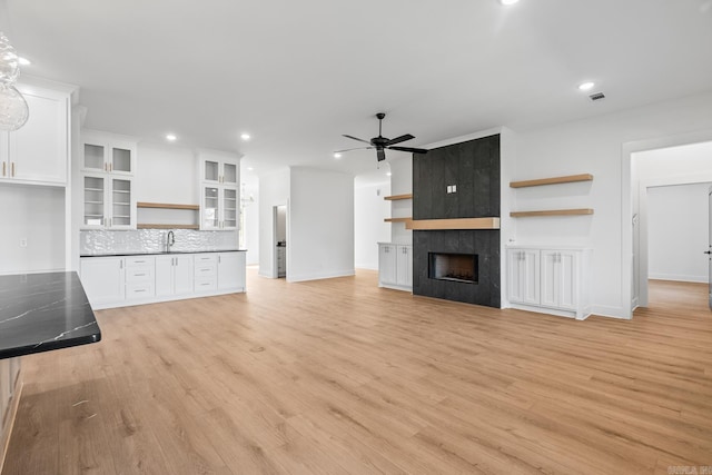 unfurnished living room with a large fireplace, light hardwood / wood-style floors, ceiling fan, and sink