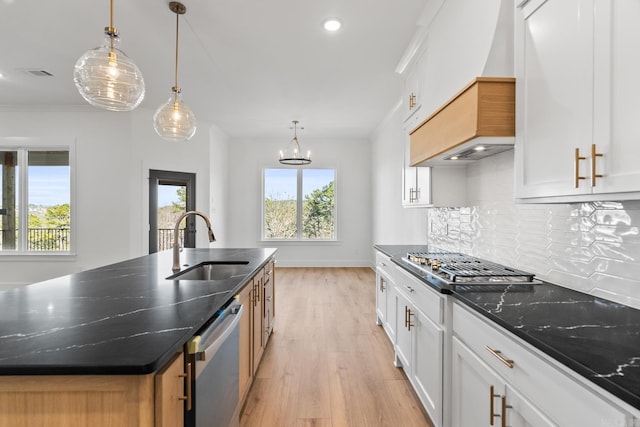 kitchen with sink, dark stone countertops, white cabinetry, hanging light fixtures, and an island with sink