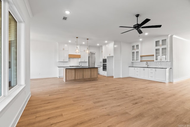 unfurnished living room featuring ceiling fan, sink, ornamental molding, and light wood-type flooring