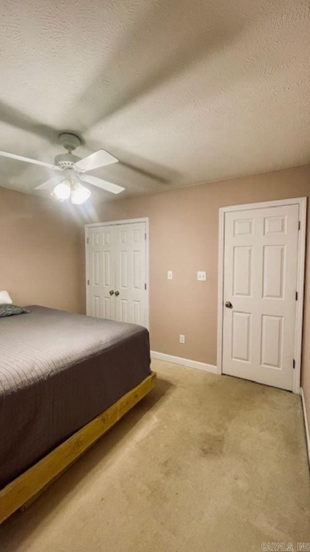 unfurnished bedroom with ceiling fan, a closet, light carpet, and a textured ceiling