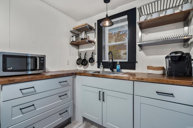 kitchen with butcher block counters, wooden walls, sink, and hanging light fixtures