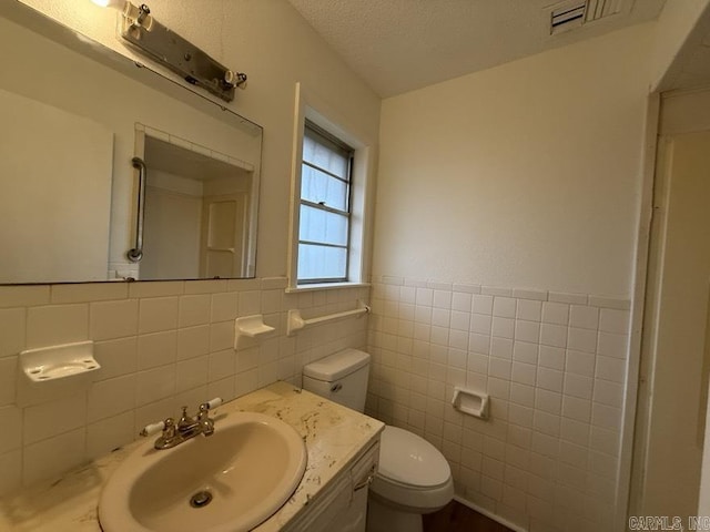 bathroom featuring a textured ceiling, vanity, tile walls, and toilet