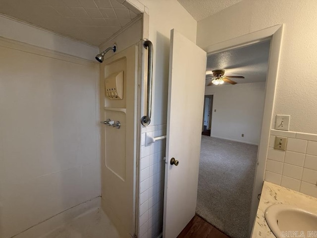 bathroom with vanity, a shower, ceiling fan, a textured ceiling, and tile walls