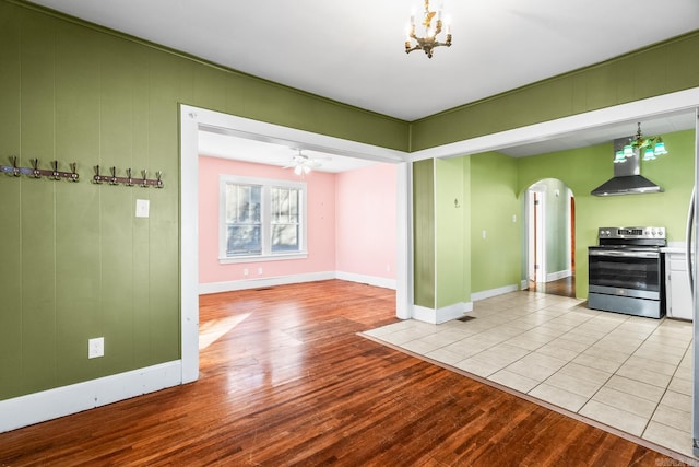 interior space featuring pendant lighting, ceiling fan with notable chandelier, wall chimney range hood, stainless steel electric range oven, and light tile patterned floors