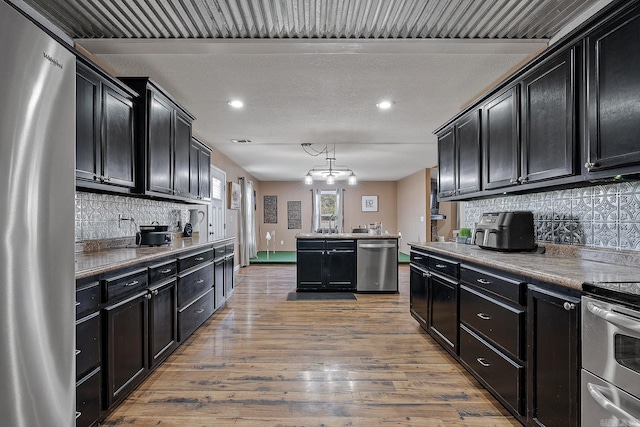 kitchen featuring stainless steel appliances, dark cabinetry, light wood-type flooring, and tasteful backsplash