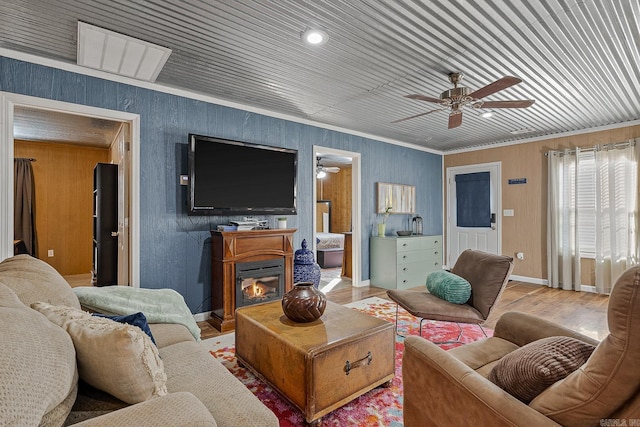 living area featuring ceiling fan, wood finished floors, baseboards, ornamental molding, and a glass covered fireplace