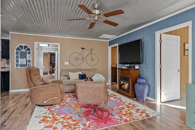 living area with ceiling fan, a glass covered fireplace, wood finished floors, and baseboards