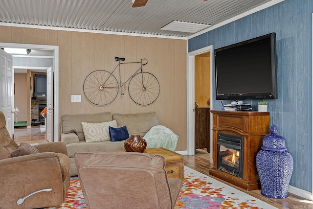 living area with wood finished floors, visible vents, baseboards, a ceiling fan, and a glass covered fireplace