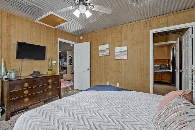 bedroom featuring a ceiling fan, attic access, and wooden walls